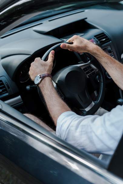 cropped view of man holding steering wheel and driving automobile  - Foto, afbeelding