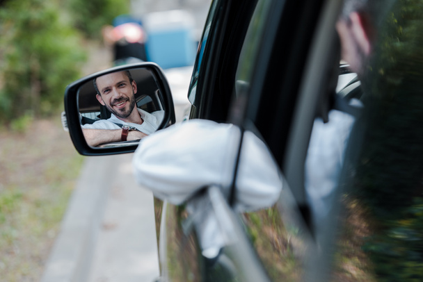 selective focus of cheerful man looking at car window and smiling in car  - Photo, Image