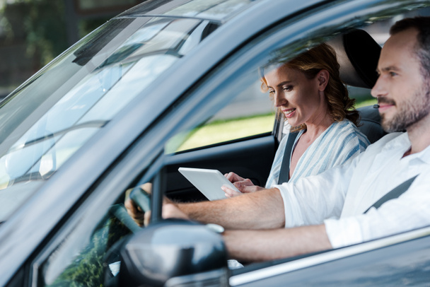 foco seletivo do homem dirigindo carro enquanto mulher segurando tablet digital
 - Foto, Imagem