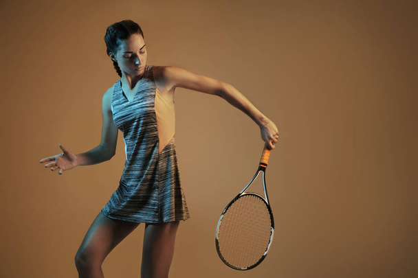 One caucasian woman playing tennis on brown background in mixed light - Foto, immagini