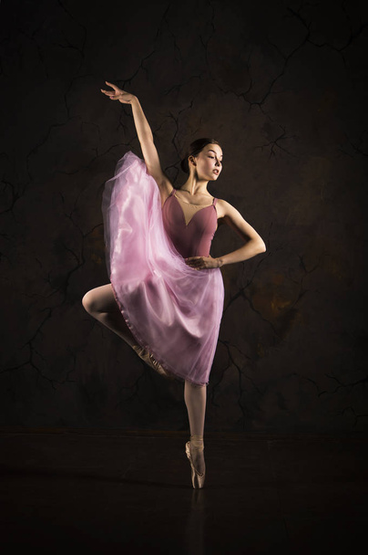 A slender girl in a pink skirt and beige top dancing ballet. - Фото, изображение