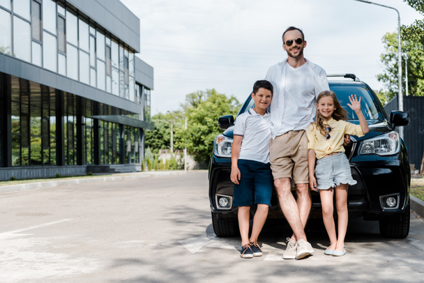 счастливый отец в солнечных очках, стоящий рядом с машиной с детьми
  - Фото, изображение