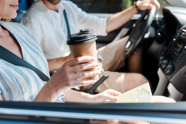 cropped view of woman sitting in car and holding paper cup near driver  - Foto, Imagen