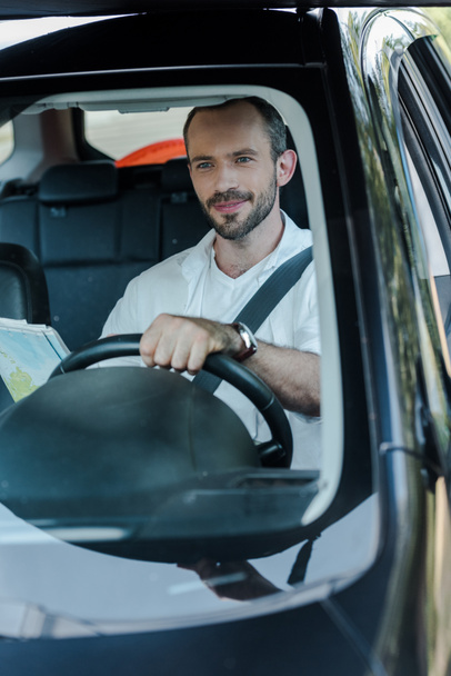 selective focus of handsome man driving car and holding map  - Fotografie, Obrázek