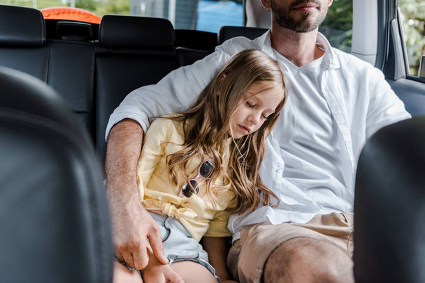 обрізаний вид на батька, сидячи в машині біля милої дочки з закритими очима
 - Фото, зображення