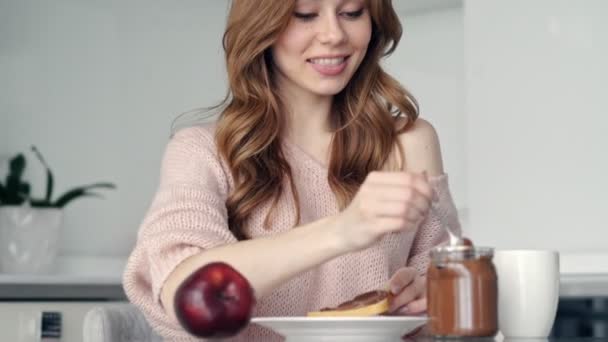 Mladá šťastná dáma příležitostně snídat v kuchyni a jíst přípitky s čokoládou doma  - Záběry, video