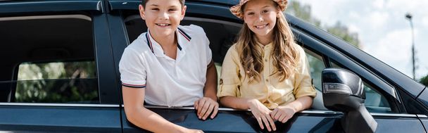 панорамний знімок щасливої сестри в солом'яному капелюсі і брат дивиться на камеру з вікон автомобіля
 - Фото, зображення