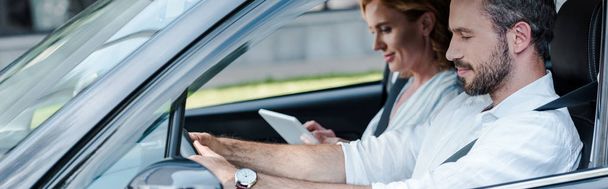 panoramic shot of man driving car near woman using digital tablet  - Foto, Imagem