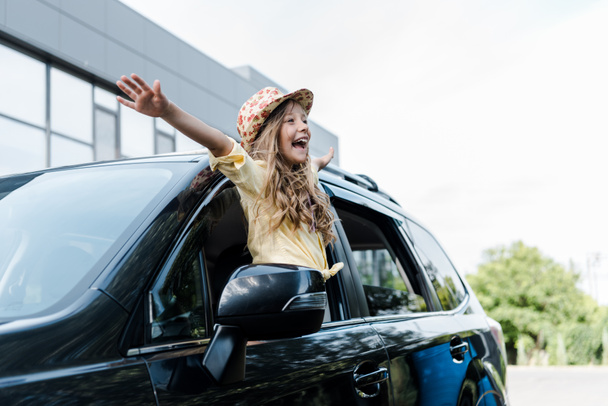 happy kid in straw hat with outstretched hands in car window  - Zdjęcie, obraz