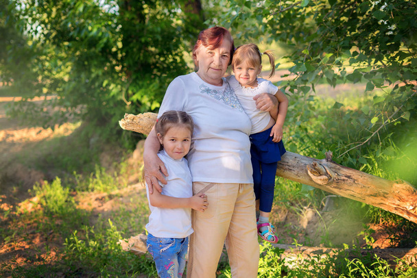 Οικογενειακό πορτρέτο της γιαγιάς με δύο εγγονές σε εξωτερικούς χώρους - Φωτογραφία, εικόνα