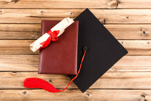 Graduation cap with diploma and book on brown wooden table - Foto, imagen