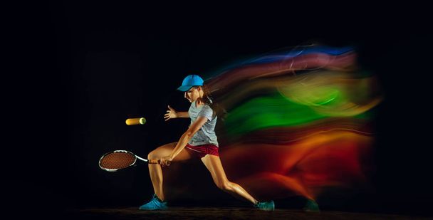One caucasian woman playing tennis on black background in mixed light - Foto, immagini