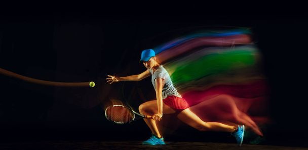 One caucasian woman playing tennis on black background in mixed light - Zdjęcie, obraz