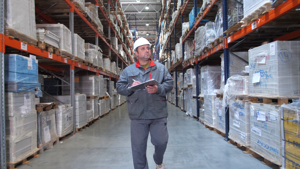 Varaston työntekijä tarkastaa korkeita hyllyjä laatikoilla. Mies kävelee putkeen kamera liikkeessä. 4K hidas Mo
 - Materiaali, video