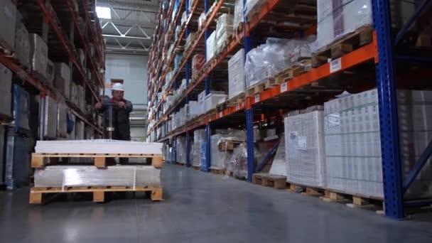 Een magazijnmedewerker draagt enorme dozen op een handmatige vorkheftruck. 4k slow mo - Video