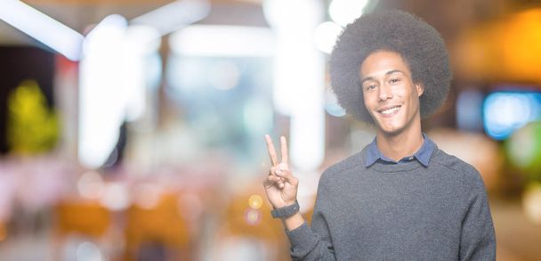 Young african american business man with afro hair smiling with happy face winking at the camera doing victory sign. Number two. - Photo, Image