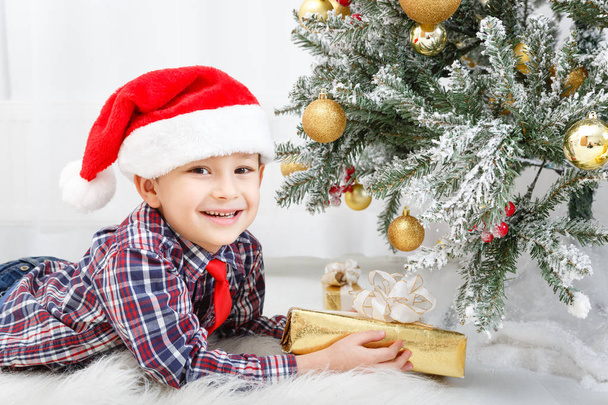 Παιδί αγόρι με χριστουγεννιάτικο δώρο κοντά σε λευκό Χριστουγεννιάτικο δέντρο - Φωτογραφία, εικόνα