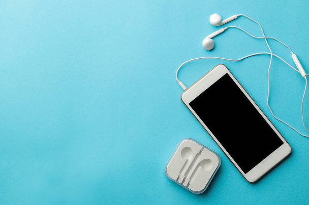 Smartphone. White phone and headphones on a bright light blue background. top view. space for text - Photo, Image