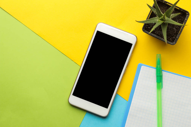 Smartphone. Teléfono blanco, bloc de notas y flor sobre un fondo multicolor brillante. Vista superior. espacio para texto
 - Foto, Imagen