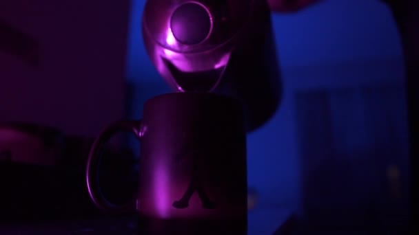 A man pours hot water from a metal kettle into a thermocup and a schematic human figure appears on it. Dark room with subdued blue light. Puzzle concept. - Záběry, video