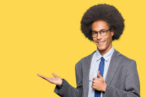 Jeune homme d'affaires afro-américain aux cheveux afro portant des lunettes montrant la main de la paume et faisant un geste correct avec les pouces levés, souriant heureux et joyeux
 - Photo, image