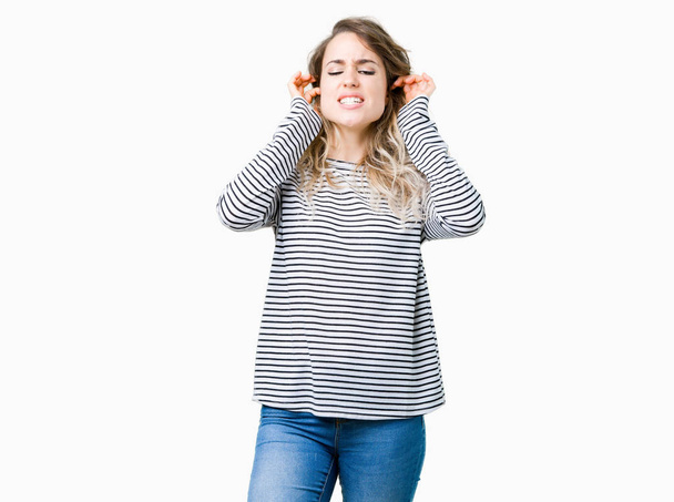 Beautiful young blonde woman wearing stripes sweater over isolated background covering ears with fingers with annoyed expression for the noise of loud music. Deaf concept. - Foto, Bild