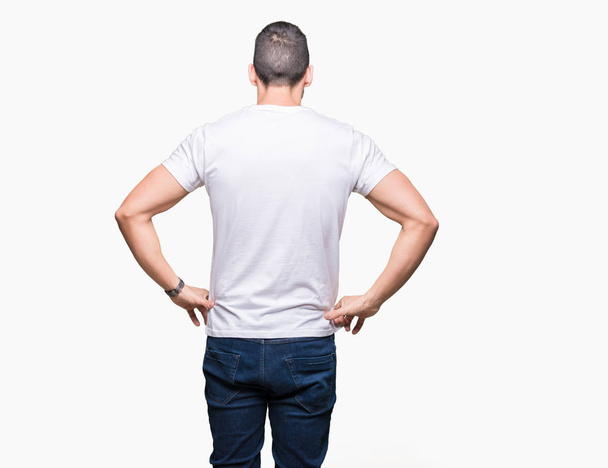 Красивий чоловік у білій футболці над білим ізольованим тлом, стоячи позаду, дивлячись з руками на тіло
 - Фото, зображення