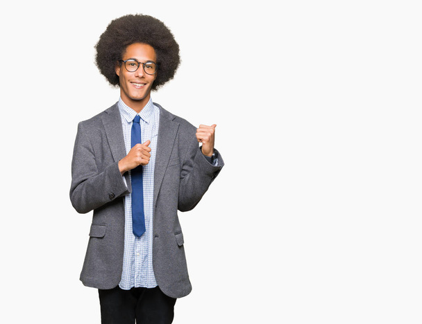 Jeune homme d'affaires afro-américain aux cheveux afro portant des lunettes pointant vers le dos avec la main et les pouces levés, souriant confiant
 - Photo, image