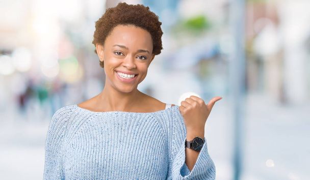 Mladá krásná africká americká žena nosí svetr izolované pozadí usmívající se smajlík pohledu a přejdete na stranu s palcem. - Fotografie, Obrázek