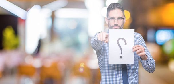 Handsome young business man holding paper with question mark over isolated background pointing with finger to the camera and to you, hand sign, positive and confident gesture from the front - Foto, immagini
