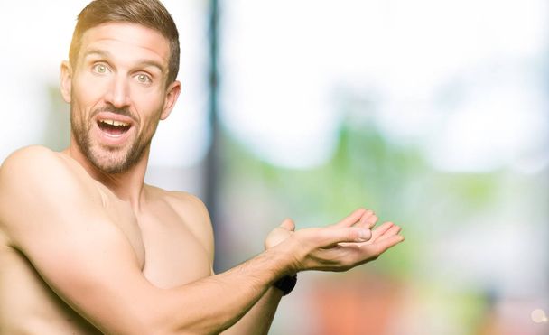 Красивый мужчина без рубашки, показывающий обнажённую грудь, указывая в сторону рукой и открытой ладонью, представляя рекламу улыбающейся счастливой и уверенной
 - Фото, изображение