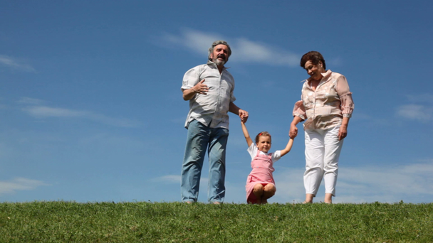 Paar steht auf Gras, Enkelin springt und hockt Händchen haltend - Filmmaterial, Video