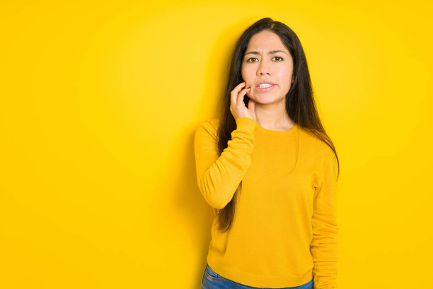 Belle femme brune sur fond jaune isolé touchant la bouche avec la main avec une expression douloureuse à cause de maux de dents ou de maladies dentaires sur les dents. Concept de dentiste
. - Photo, image