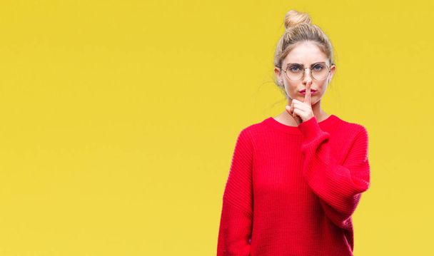 Jonge mooie blonde vrouw dragen rode trui en glazen over geïsoleerde achtergrond vragen stil met de vinger op de lippen te zijn. Stilte en geheime concept. - Foto, afbeelding