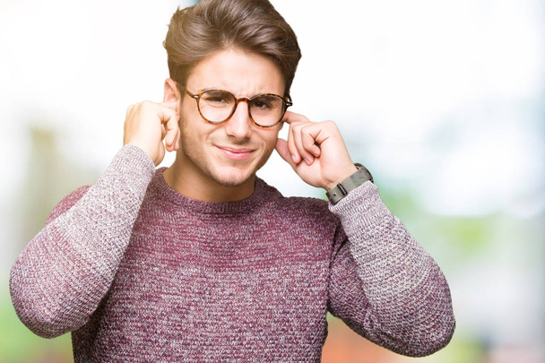 Jonge knappe man met bril op geïsoleerde achtergrond die betrekking hebben op oren met vingers met geërgerd expressie voor het geluid van luide muziek. Dove concept. - Foto, afbeelding