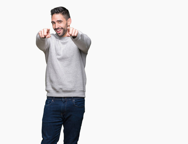 junger gutaussehender Mann, der Sweatshirt über isoliertem Hintergrund trägt und mit den Fingern auf dich und die Kamera zeigt, positiv und fröhlich lächelt - Foto, Bild