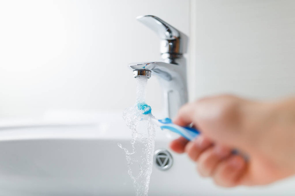 hand holding toothbrush under flowing water from faucet - Photo, image