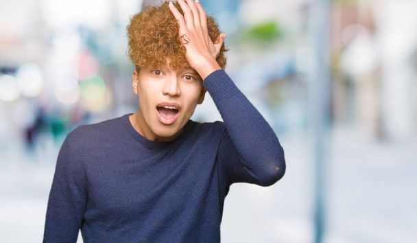 Young handsome man with afro hair surprised with hand on head for mistake, remember error. Forgot, bad memory concept. - Foto, Imagem
