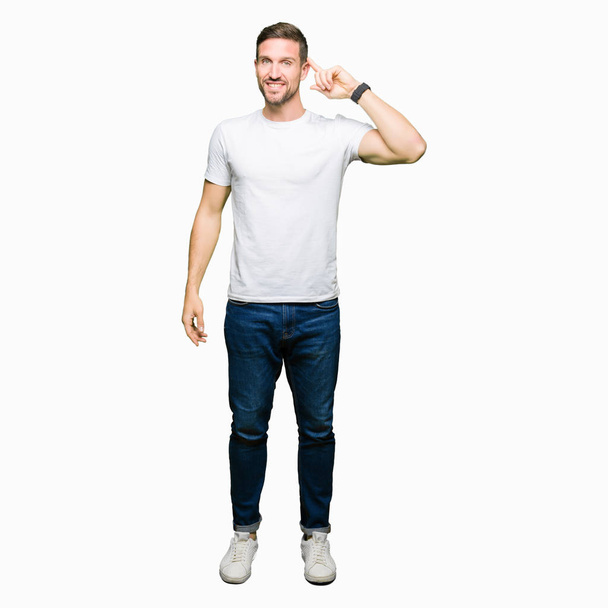Pohledný muž nosí ležérní bílé tričko s úsměvem ukazující na hlavě s jedním prstem, skvělý nápad nebo myšlení, dobrou paměť - Fotografie, Obrázek