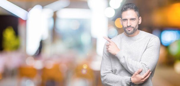 Young handsome man wearing sweatshirt over isolated background Pointing with hand finger to the side showing advertisement, serious and calm face - Foto, immagini