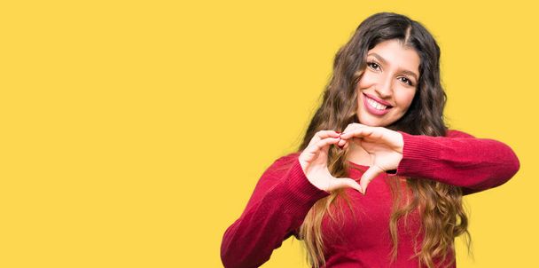 Mooie jongedame dragen rode trui glimlachend in liefde met hartsymbool en vorm met de handen. Romantische concept. - Foto, afbeelding