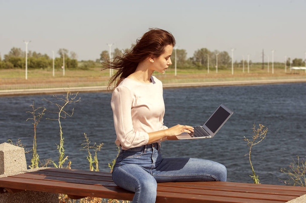 Young woman with a laptop on a park bench - Fotó, kép