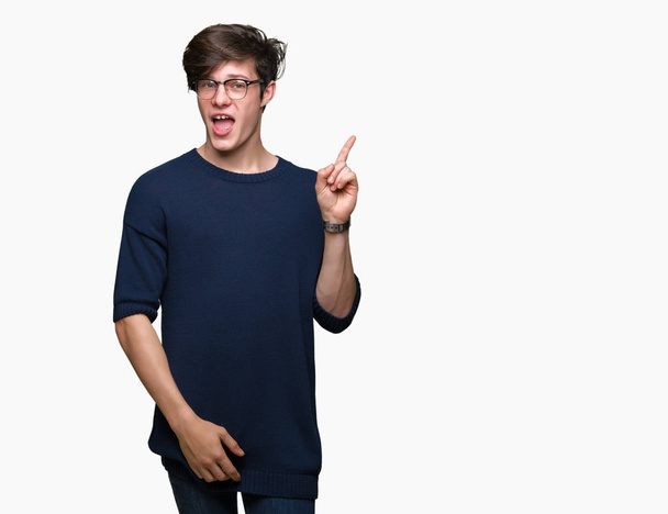 Young handsome man wearing glasses over isolated background with a big smile on face, pointing with hand and finger to the side looking at the camera. - Foto, Imagen