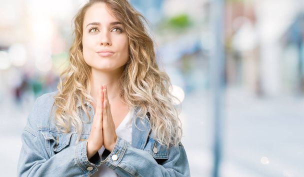 Bella giovane donna bionda che indossa giacca di jeans su sfondo isolato pregando con le mani insieme chiedendo perdono sorridente fiducioso
. - Foto, immagini