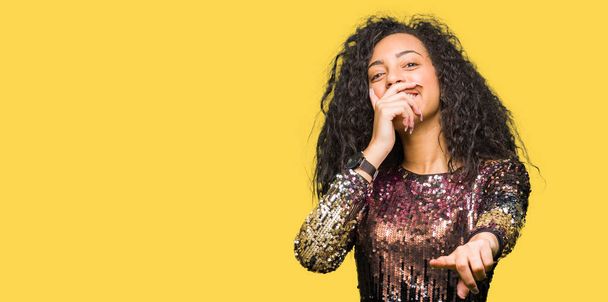 Young beautiful girl with curly hair wearing night party dress Laughing of you, pointing to the camera with finger hand over mouth, shame expression - Foto, Imagem