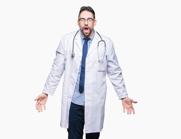 Pohledný mladý lékař muže nad izolované pozadí v šoku obličeje, skeptický a sarkastický, překvapil s otevřenými ústy - Fotografie, Obrázek