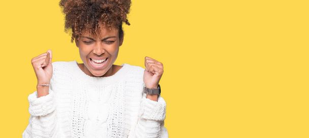 腕の成功のために興奮して孤立した背景に冬のセーターを着ている美しい若いアフリカ系アメリカ人女性は、祝う勝利笑顔を発生します。勝者の概念. - 写真・画像