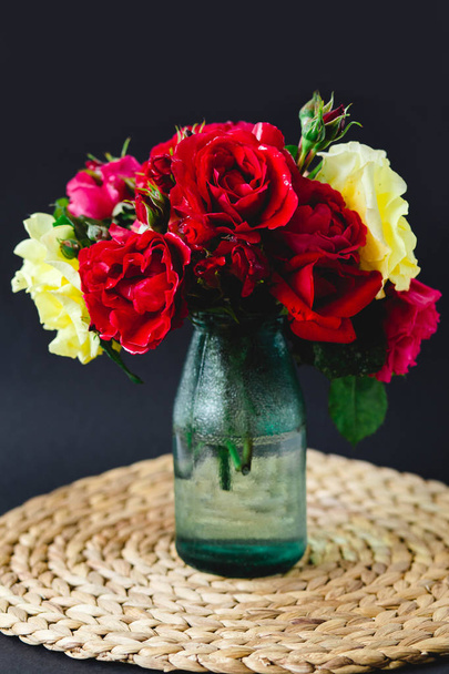Verbluffende samenstelling van kleurrijke rozen in een glazen vaas op een rieten servet - Foto, afbeelding