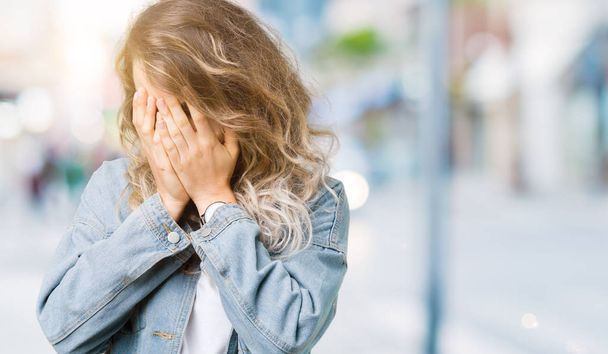Красивая молодая блондинка в джинсовой куртке на изолированном фоне с грустным лицом, прикрывающим лицо руками во время плача. Концепция депрессии
. - Фото, изображение