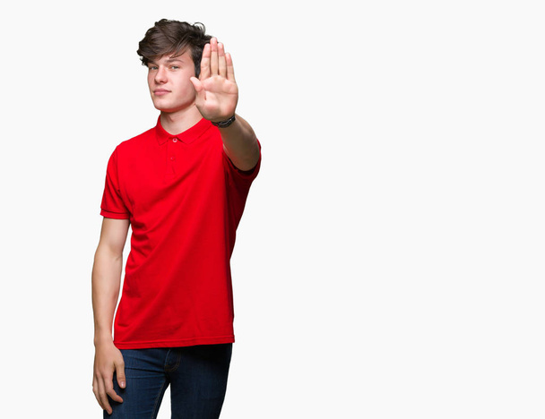Młody przystojny mężczyzna ubrany w czerwony t-shirt na białym tle robi przestać śpiewać z dłoni. Wyrażenie ostrzegawcze z negatywnym i poważnym gestem na twarzy. - Zdjęcie, obraz